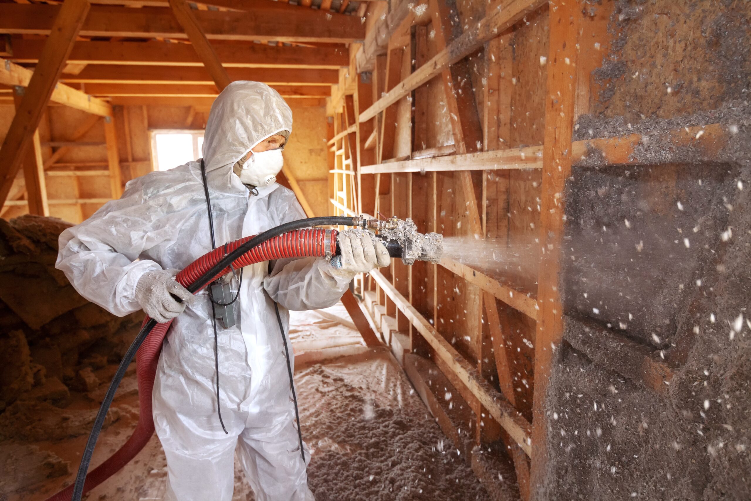 man adding sprayed in cellulose insulation to an attic